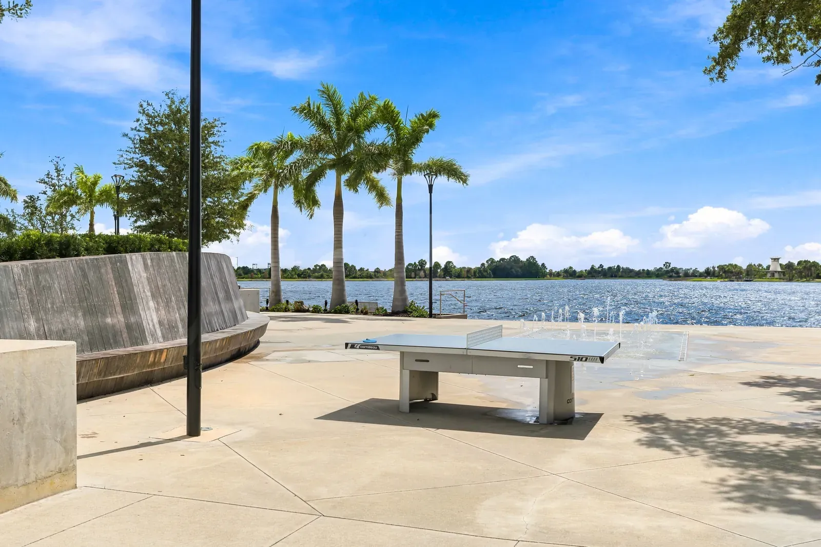 Outdoor ping-pong table and splash-pad fountains on a lakefront plaza lined with royal palms in Wellen Park